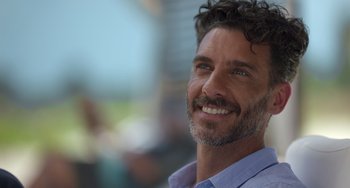 Movie still from “40 Years Young” (2022), directed by Pietro Loprieno – A person with a beard smiling; Close Up shot, Over the shoulder angle