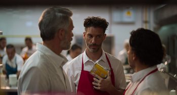 Movie still from “40 Years Young” (2022), directed by Pietro Loprieno – A group of people standing around talking to each other; Medium shot, Over the shoulder angle