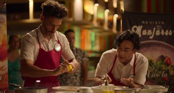 Movie still from “40 Years Young” (2022), directed by Pietro Loprieno – Two men in red aprons preparing food in a kitchen; Medium shot, High angle