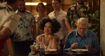 Movie still from “40 Years Young” (2022), directed by Pietro Loprieno – A woman sitting at a table with a plate of food; Medium shot, Over the shoulder angle