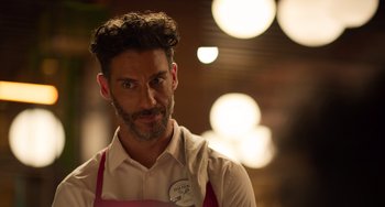 Movie still from “40 Years Young” (2022), directed by Pietro Loprieno – A man in a white shirt and a pink apron; Close Up shot, Over the shoulder angle
