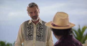 Movie still from “40 Years Young” (2022), directed by Pietro Loprieno – A man wearing a hat and a white shirt is talking to another man; Medium shot, Over the shoulder angle