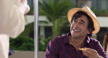 Movie still from “40 Years Young” (2022), directed by Pietro Loprieno – A man wearing a straw hat is eating a banana; Close Up shot, Over the shoulder angle