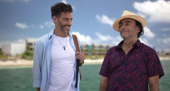 Movie still from “40 Years Young” (2022), directed by Pietro Loprieno – Two men standing next to each other on the beach; Medium shot, Over the shoulder angle