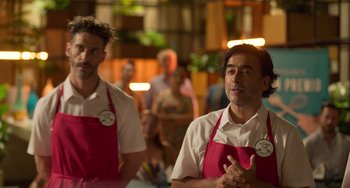Movie still from “40 Years Young” (2022), directed by Pietro Loprieno – Two men in red aprons standing next to each other; Medium shot, Over the shoulder angle