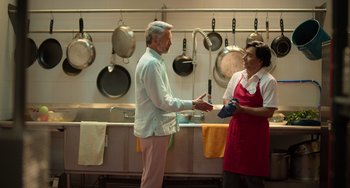 Movie still from “40 Years Young” (2022), directed by Pietro Loprieno – A man and a woman are talking in a kitchen; Medium shot, Over the shoulder angle
