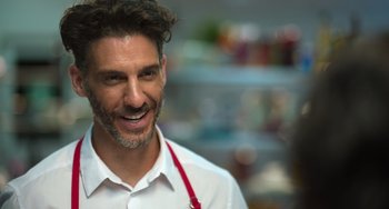 Movie still from “40 Years Young” (2022), directed by Pietro Loprieno – A man wearing a white shirt and a red tie smiling; Close Up shot, Over the shoulder angle