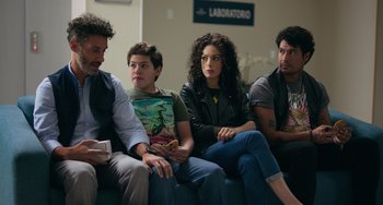 Movie still from “40 Years Young” (2022), directed by Pietro Loprieno – A group of people sitting next to each other on a couch; Medium shot, Over the shoulder angle