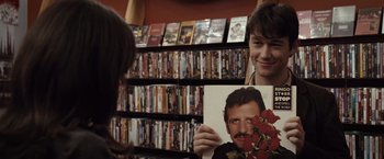 Movie still from “500 Days of Summer” (2009), directed by Marc Webb – A man holding up a picture in front of a shelf full of dvds; Close Up shot, Over the shoulder angle