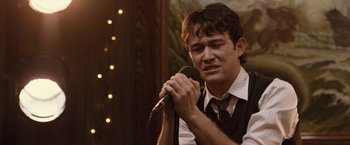 Movie still from “500 Days of Summer” (2009), directed by Marc Webb – A man holding a microphone and looking sad; Close Up shot, Over the shoulder angle