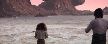 Movie still from “65” (2023), directed by Bryan Woods – A woman standing in the water looking at the ocean; Extreme Wide shot, Over the shoulder angle