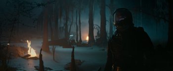 Movie still from “65” (2023), directed by Bryan Woods – A man in a space suit standing in the woods; Wide shot, Over the shoulder angle