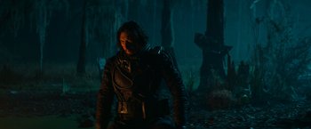 Movie still from “65” (2023), directed by Bryan Woods – A man in a black jacket standing next to a tree; Wide shot, Low angle