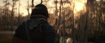 Movie still from “65” (2023), directed by Bryan Woods – A person wearing a black jacket standing next to trees; Medium shot, Over the shoulder angle