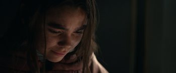 Movie still from “65” (2023), directed by Bryan Woods – A young woman with long brown hair looking down at her face; Close Up shot, Over the shoulder angle