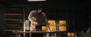 Movie still from “65” (2023), directed by Bryan Woods – A man standing in front of a counter holding a knife; Medium shot, Low angle