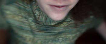 Movie still from “65” (2023), directed by Bryan Woods – A woman wearing a neck scarf with a blurry background; Extreme Close Up shot, Overhead angle