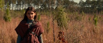 Movie still from “65” (2023), directed by Bryan Woods – A young girl in a field with trees in the background; Medium shot, Low angle