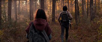 Movie still from “65” (2023), directed by Bryan Woods – A man and a woman walking through the woods; Wide shot, Over the shoulder angle