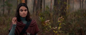 Movie still from “65” (2023), directed by Bryan Woods – A woman in a red cape standing in the woods; Medium shot, Over the shoulder angle