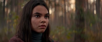 Movie still from “65” (2023), directed by Bryan Woods – A young woman with long brown hair wearing a scarf looking to her left; Close Up shot, Low angle