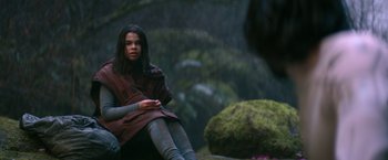 Movie still from “65” (2023), directed by Bryan Woods – A woman sitting on a rock in the woods; Medium shot, Over the shoulder angle