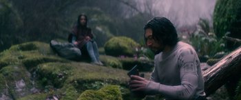 Movie still from “65” (2023), directed by Bryan Woods – A man sitting on the ground looking at his cell phone; Medium shot, Over the shoulder angle