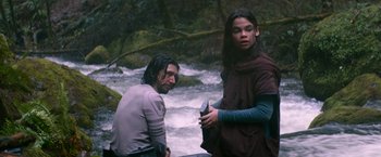 Movie still from “65” (2023), directed by Bryan Woods – A man and a woman standing next to each other near a river; Medium shot, Low angle