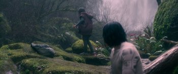 Movie still from “65” (2023), directed by Bryan Woods – Two people walking through a misty forest on rocks; Wide shot, High angle
