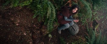 Movie still from “65” (2023), directed by Bryan Woods – A woman sitting on the ground in the woods; Wide shot, Overhead angle