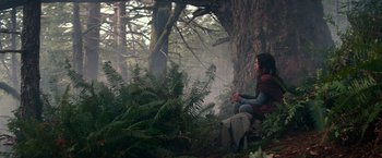 Movie still from “65” (2023), directed by Bryan Woods – A person sitting in the middle of a forest; Wide shot, Low angle