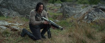 Movie still from “65” (2023), directed by Bryan Woods – A man kneeling down holding a rifle in a field; Medium shot, Low angle