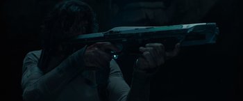 Movie still from “65” (2023), directed by Bryan Woods – A person holding a gun in a dark room; Close Up shot, High angle