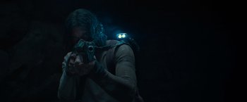 Movie still from “65” (2023), directed by Bryan Woods – A man holding a gun in a dark room; Medium shot, Low angle