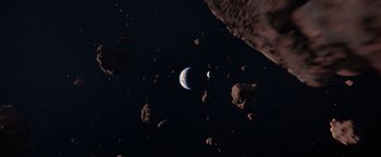 Movie still from “65” (2023), directed by Bryan Woods – An earth and moon in a space with asteroids; Extreme Wide shot, Overhead angle