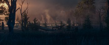 Movie still from “65” (2023), directed by Bryan Woods – Smoke billows from a fire in a wooded area at night; Extreme Wide shot, High angle