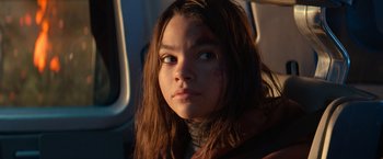 Movie still from “65” (2023), directed by Bryan Woods – A young girl with long brown hair looking at the camera; Close Up shot, Over the shoulder angle