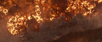 Movie still from “65” (2023), directed by Bryan Woods – A fire is burning in the sky and the trees are in the background; Extreme Wide shot, Overhead angle