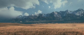 Movie still from “65” (2023), directed by Bryan Woods – A large open field with mountains in the background; Extreme Wide shot, High angle