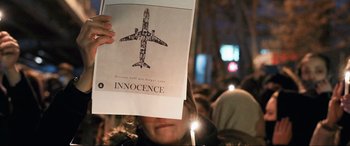 Movie still from “752 Is Not a Number” (2022), directed by Babak Payami – A person holding up a sign with a drawing of an airplane on it; Extreme Wide shot, Overhead angle