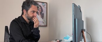 Movie still from “752 Is Not a Number” (2022), directed by Babak Payami – A man sitting in front of a picture of a woman; Medium shot, Over the shoulder angle