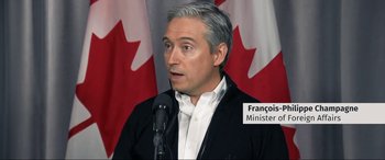 Movie still from “752 Is Not a Number” (2022), directed by Babak Payami – A man in a black jacket is talking into a microphone; Close Up shot, Over the shoulder angle