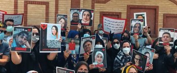 Movie still from “752 Is Not a Number” (2022), directed by Babak Payami – A group of people holding up signs with pictures of missing people on them; Medium shot, High angle