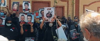 Movie still from “752 Is Not a Number” (2022), directed by Babak Payami – A group of people gathered outside holding up pictures; Medium shot, Overhead angle