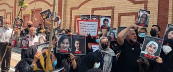 Movie still from “752 Is Not a Number” (2022), directed by Babak Payami – A group of people holding up signs in front of a brick wall; Medium shot, Overhead angle