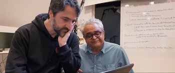 Movie still from “752 Is Not a Number” (2022), directed by Babak Payami – Two men looking at a computer screen together; Medium shot, Over the shoulder angle