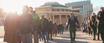 Movie still from “752 Is Not a Number” (2022), directed by Babak Payami – A group of people standing in a line outside a building; Extreme Wide shot, High angle