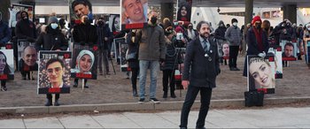 Movie still from “752 Is Not a Number” (2022), directed by Babak Payami – A man walking down the street while holding a microphone; Wide shot, Over the shoulder angle
