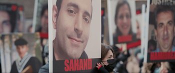 Movie still from “752 Is Not a Number” (2022), directed by Babak Payami – A woman holding a sign with a picture of a man; Extreme Close Up shot, Overhead angle