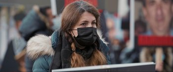 Movie still from “752 Is Not a Number” (2022), directed by Babak Payami – A woman wearing a black face mask while sitting outside; Close Up shot, Low angle